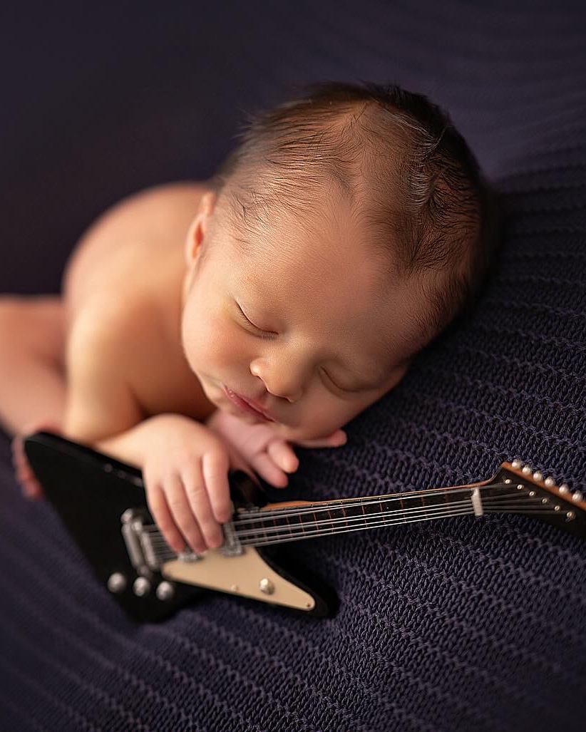Recém-nascido dormindo ao lado de uma mini guitarra